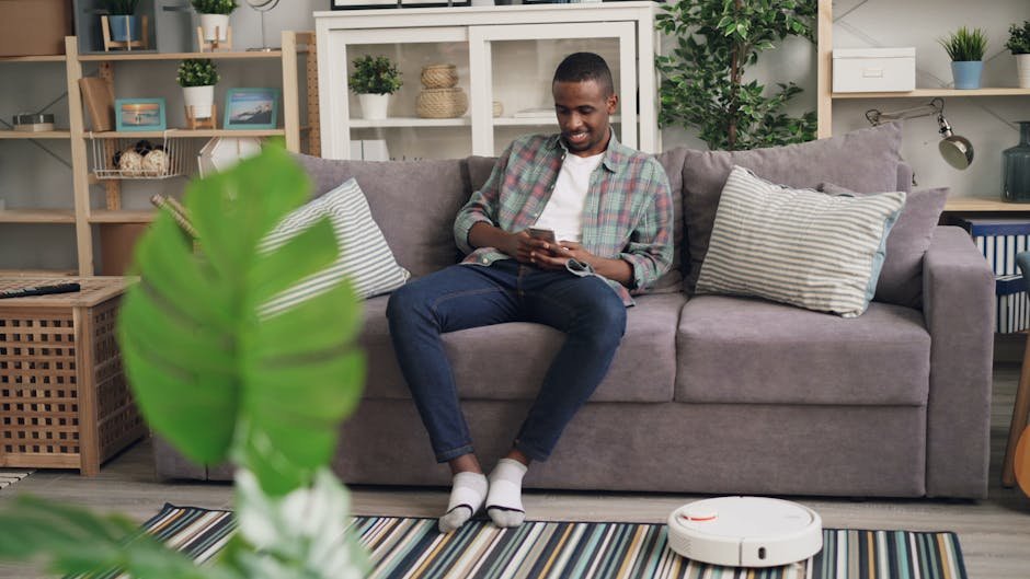 Casual home interior with man sitting on sofa, using smartphone and smiling.