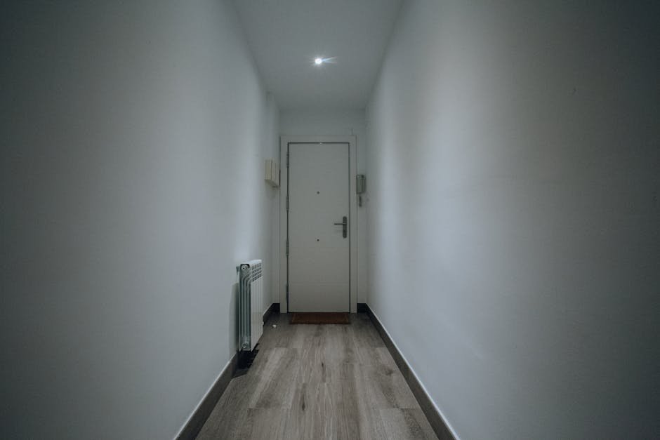 A simple and clean indoor hallway featuring a closed door and wooden flooring.