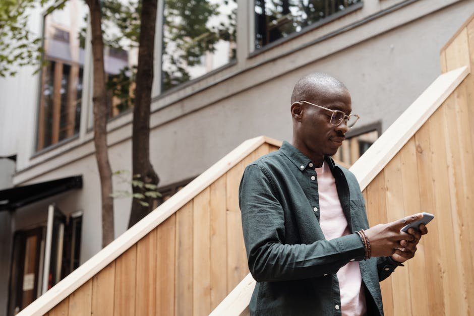 African American man texting on smartphone outdoors wearing stylish eyeglasses.