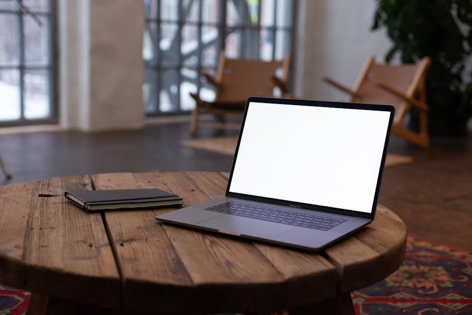 An open laptop on a rustic wooden table with a notebook, in a cozy indoor setting with natural light.