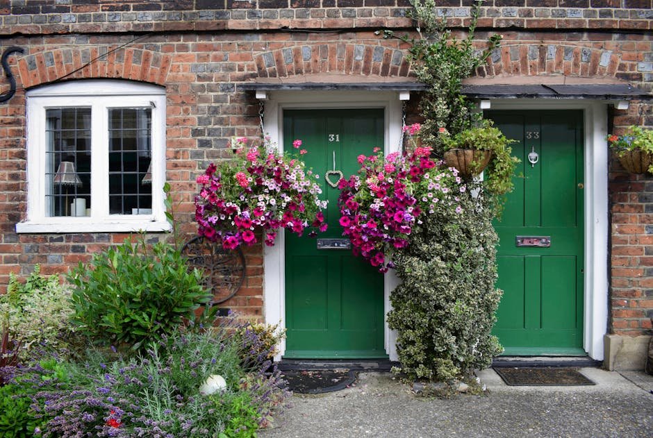 Front view of a residential brick house with green doors and vibrant flower arrangements.