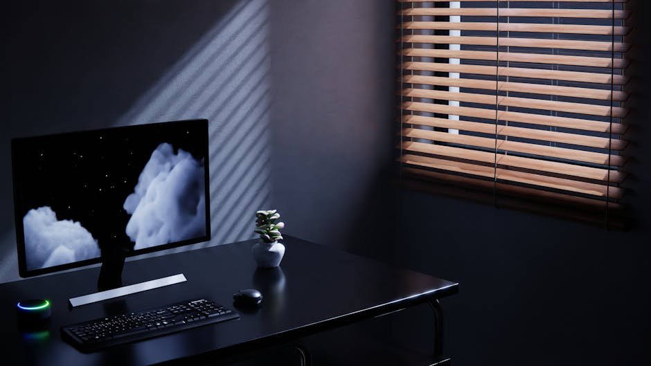 Minimalist workspace featuring a monitor, keyboard, and window blinds casting shadows.