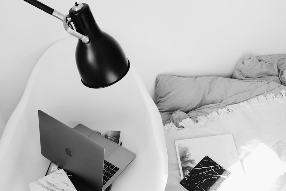 A cozy monochrome workspace with a laptop on a chair beside a bed, ideal for remote work.