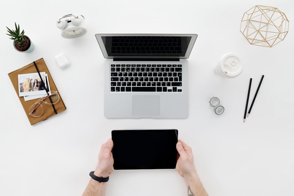 Flat lay of a modern workspace with laptop, tablet, and stationary on a white desk.