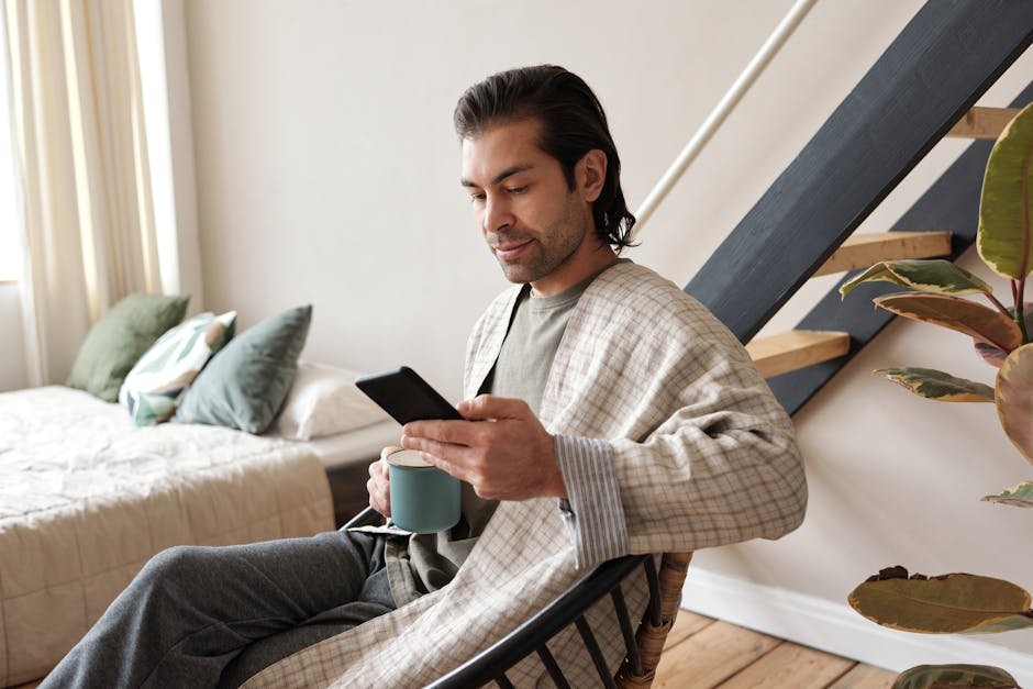 Adult man enjoying relaxation time indoors, drinking coffee and using smartphone.