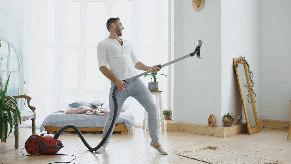 Man enjoying cleaning with vacuum, singing like a rockstar in bright bedroom.
